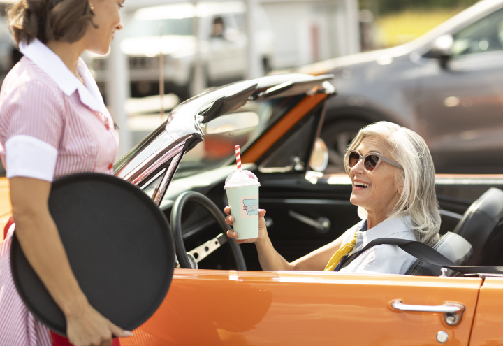 Woman in orange convertible with milkshake