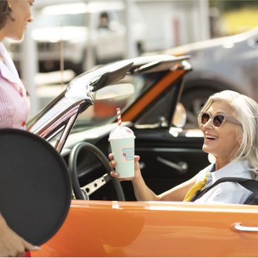 Woman in orange convertible with milkshake