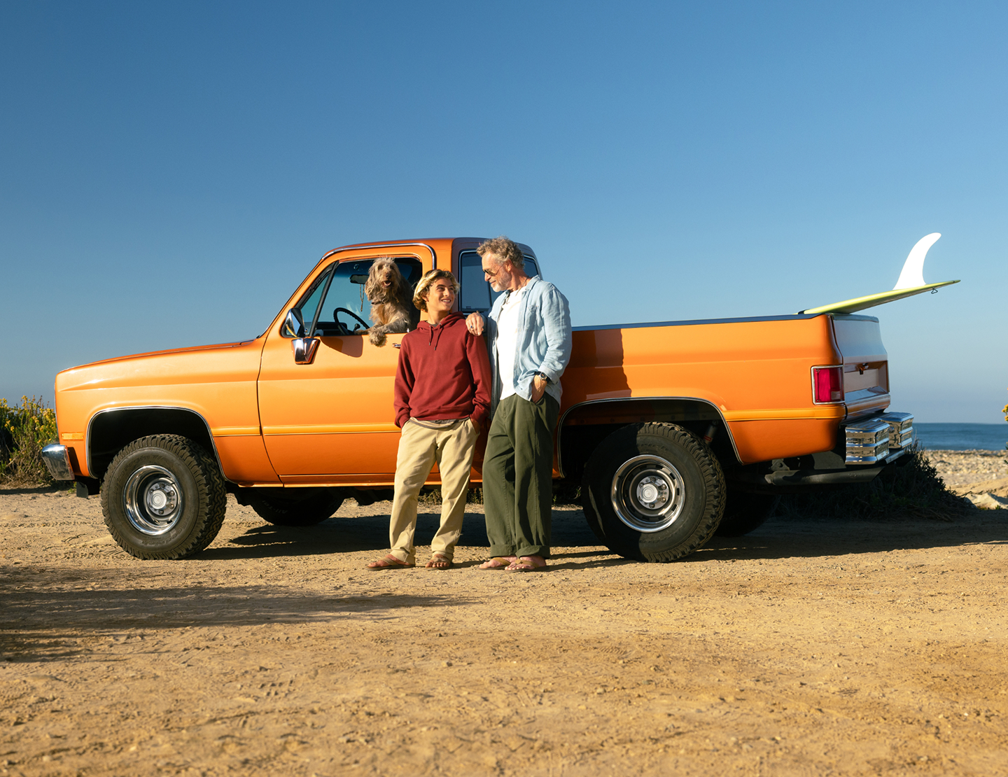 Grandfather and grandson standing in front of an orange pickup truck