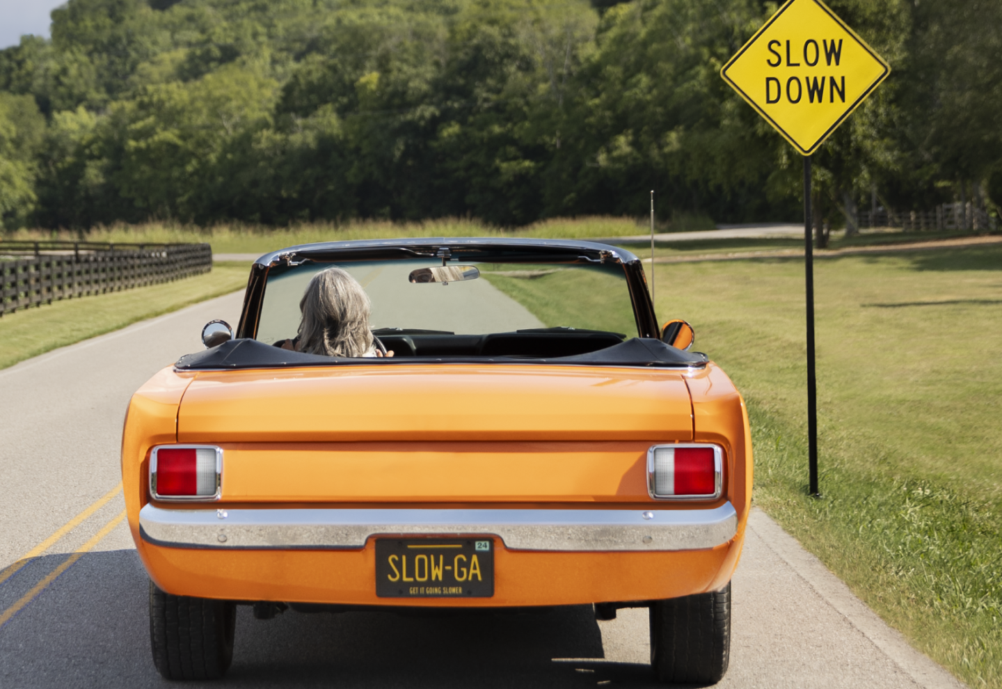 An orange convertible in front of a 'Slow Down' sign