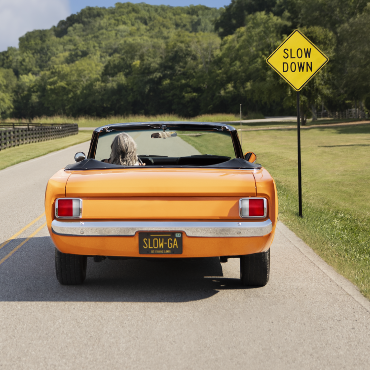 An orange convertible in front of a 'Slow Down' sign